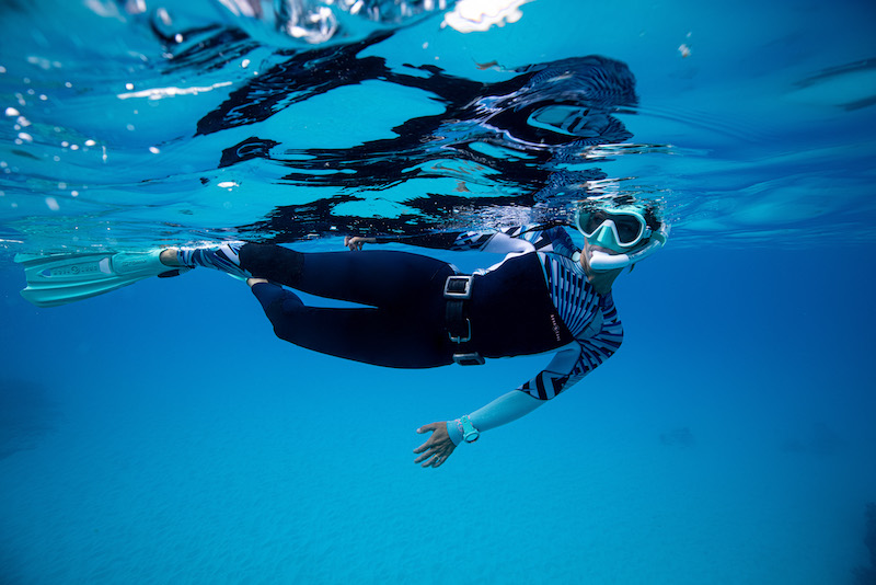 Female diver in snorkel gear below the ocean surface.