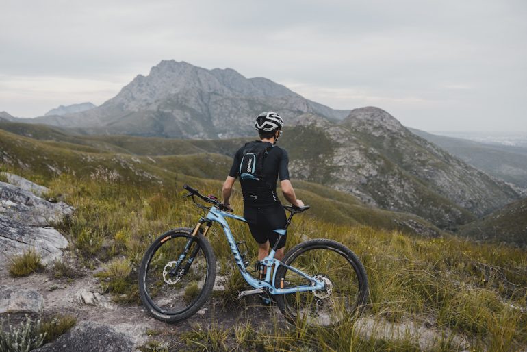 Mountain biker standing near his bike on a mountain trail with the USWE pack