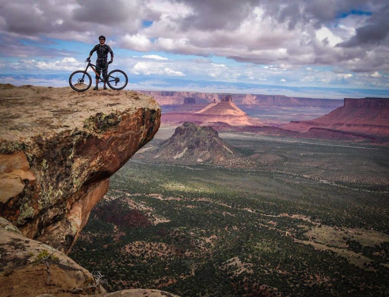 Mountain biker stands on a rock overhang in Moab