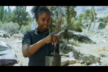 Young lady using a water filtration system at her campsite