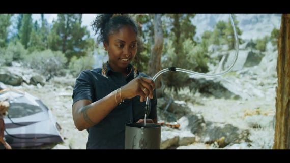 Young lady using a water filtration system at her campsite