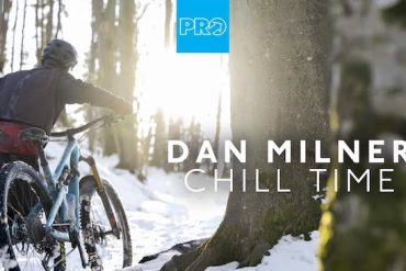 Dan Milner pushing his bike through the alpine winter snow of the Alps surrounded by trees