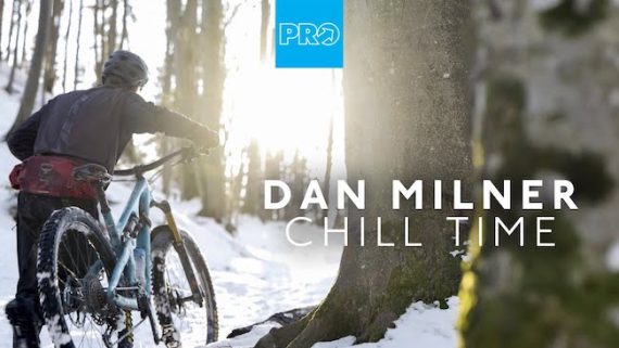 Dan Milner pushing his bike through the alpine winter snow of the Alps surrounded by trees