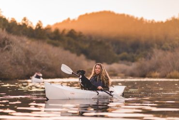 A girl paddling her Oru Kayak with her dog on a calm lake