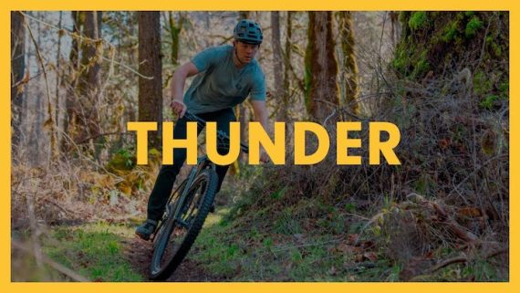 A young man riding his Breezer Thunder mountain bike around a corner on a grassy trail