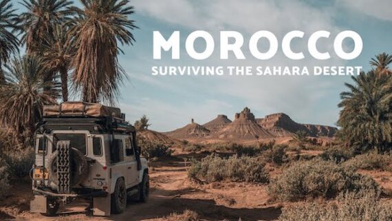 A Land Rover Defender crosses a dusty path in Morocco's Sahara Desert.