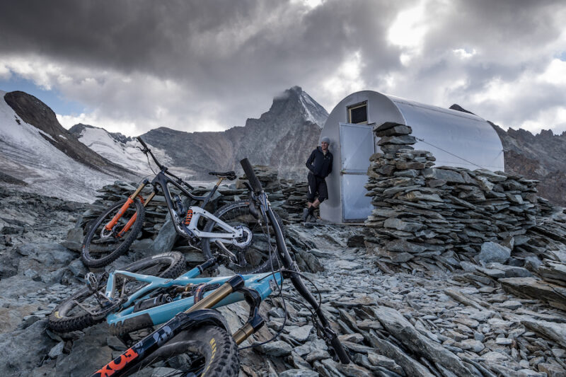 A pro rider and photographer stand beside their bikes in the Italian Alps.