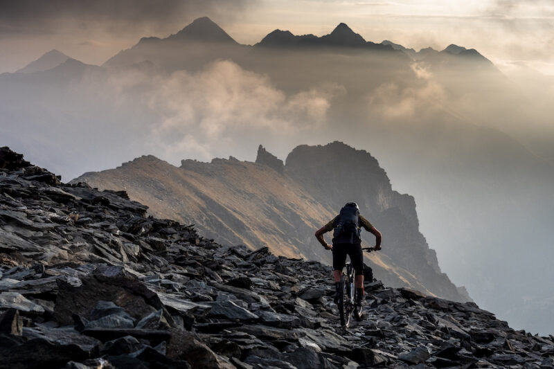 A mountain biker rides off into the sunset on a rocky trail in the Italian Alps