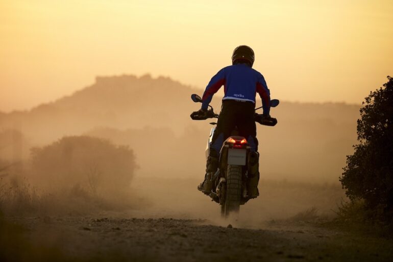 An rider on his Aprilia motorcycle in the desert at sunset