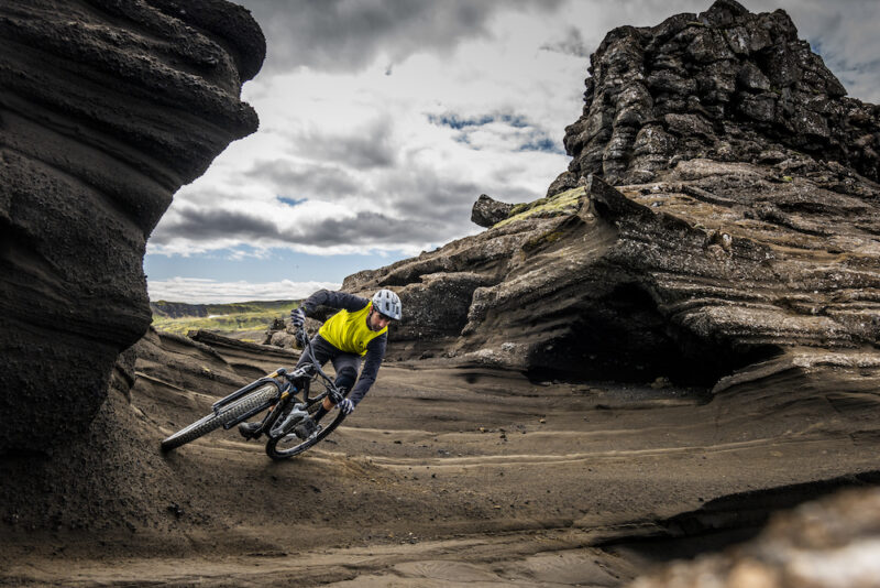 A mountain biker pedals along a vertical rock wall in Iceland.