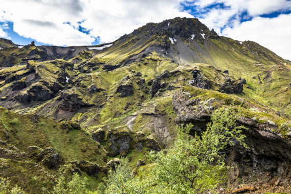 A mountain biker poses with his bike next to a geothermal pool with steam rising from the water in Iceland.