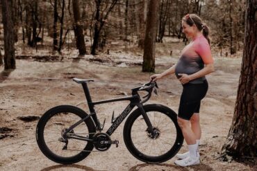 Pro cyclist Nikky Alberts stand beside her road bike in her kit during her pregnancy.