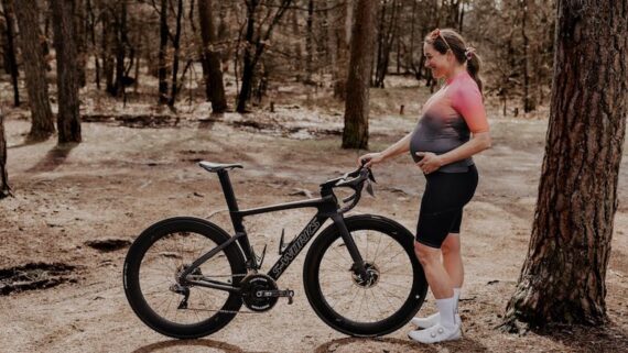 Pro cyclist Nikky Alberts stand beside her road bike in her kit during her pregnancy.