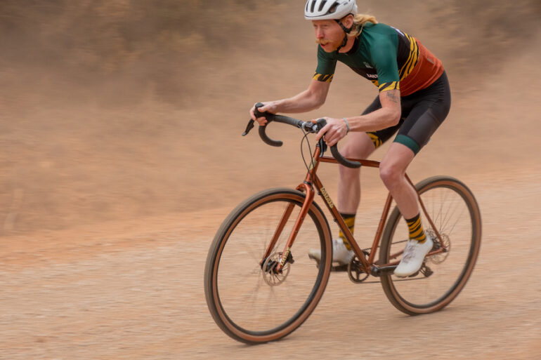 A male cyclist riding The Wild Bicycle Co. Rambler SL on a dusty dirt road at speed.