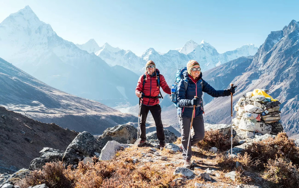 A man and a woman in hiking gear with poles atop a mountain peak