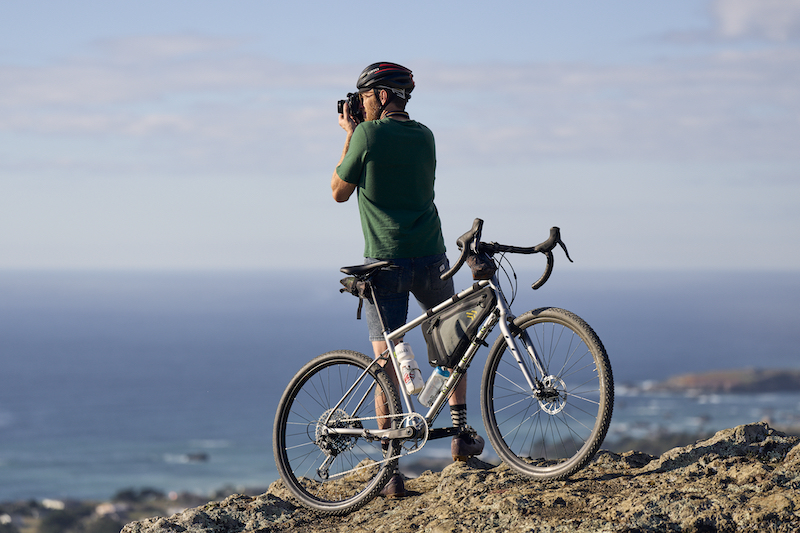 A cyclist with his camera and Marin Four Corners on a rocky lookout.