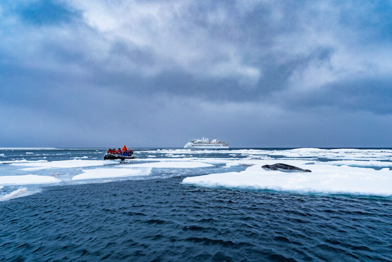 A group of travelers on a raft among sea ice and a lone seal while exploring the Arctic with adventuresmith explorations Antarctica.