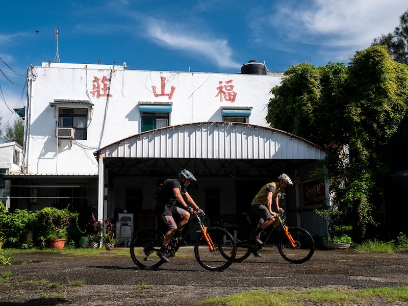 Two mountain bikers riding the unpaved streets of Taiwan's rural towns.