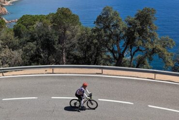 A female road cyclist riding a coastal road on the Girona cycling tour.