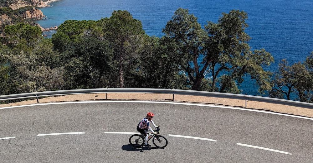 A female road cyclist riding a coastal road on the Girona cycling tour.