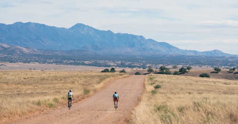 Two cyclists on a vast dirt road in the high desert of Arizona.