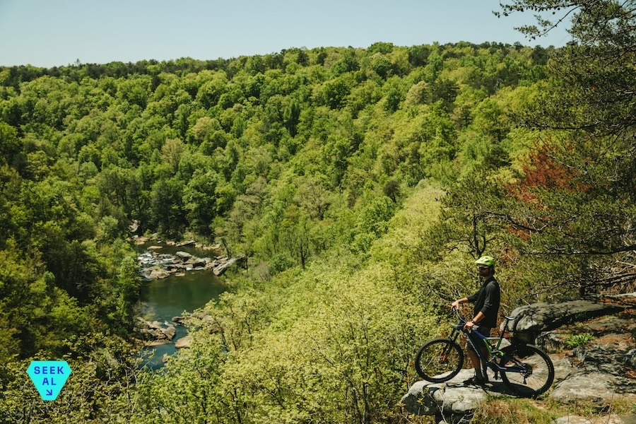 A mountain biker stands next to his bike on a rocky outlook in the Alabama wilderness