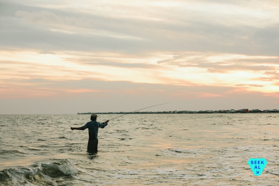 A fisherman stands in knee-deep water holding his fishing pole along Alabama's Gulf Coast.